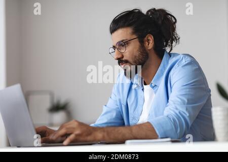 Young Eastern Employee Working On Laptop At Desk In Office Stockfoto