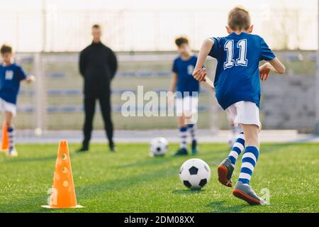 Gruppe von jungen Jungs mit Trainer üben Fußball auf dem Feld. Kinder laufen Fußballbälle auf Trainingseinheit Stockfoto