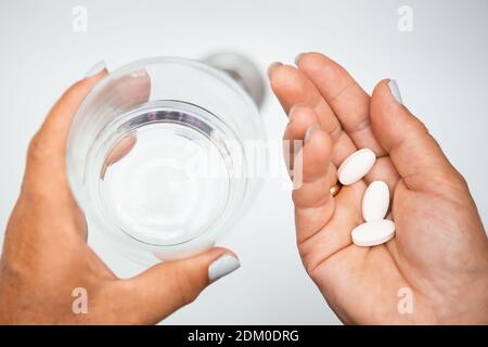 Female elderly hand with pills medicine tablets and glass of water against white sinks with fresh water. Senior woman taking pills at home, closeup. D Stock Photo