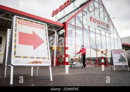 Grevenbroich, Deutschland. Dezember 2020. Ein Toom Hausverbesserungs-Store-Mitarbeiter schiebt einen Warenkorb vorbei am Baumarkt, während ein Schild mit der Aufschrift "Pickup Station" im Vordergrund zu sehen ist. Seit dem 16. Dezember 2020 ist landesweit eine harte Sperre in Kraft. Baumärkte sind jetzt nicht mehr erlaubt, für Wohnkunden zu öffnen, wie sie in der Vergangenheit haben. Vorbestellungen können jedoch noch persönlich abgeholt werden. Quelle: Jonas Güttler/dpa/Alamy Live News Stockfoto