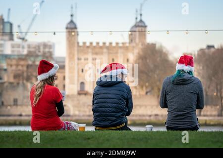 Weihnachten 2020: Freunde, die Weihnachtsmützen tragen, warten am Nachmittag an der Promenade des Queen's Walk gegenüber dem Tower of London Gebäude, London, UK. Stockfoto