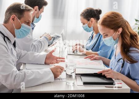 Multiethnisches Krankenhauspersonal, das am Arbeitsplatz mit Papieren, Geräten und Gläsern Wasser im Krankenhaus arbeitet Stockfoto