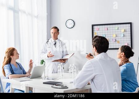 Multiethnisches Krankenhauspersonal, das mit Laptop und Papiermappe arbeitet Klinik Stockfoto