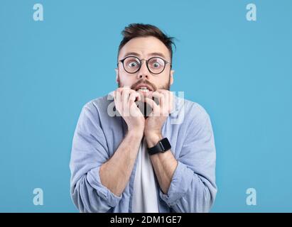 Angst Millennial Kerl beißen Nägel in Panik über blauen Studio Hintergrund Stockfoto