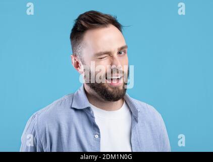 Selbstbewusst gut aussehende kaukasischen Mann winken und lächeln bei Kamera auf Blauer Studiohintergrund Stockfoto