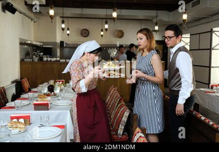 Im Restaurant Krimtartar: Kellnerin in Tartar-Heimatkleid, die in der Mitte eines Speisesaals mit Geschirr in den Händen steht, Manager, die mit ihr sprechen. S Stockfoto