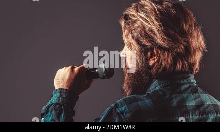 Männlicher Gesang mit Mikrofonen. Mann mit einem Bart, der ein Mikrofon hält und singt. Bärtiger Mann in Karaoke singt ein Lied in ein Mikrofon Stockfoto