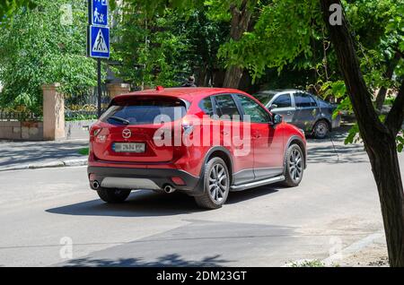 Nikolaev, Ukraine - 31. Mai 2020: Roter Crossover Mazda CX-5 fährt auf einer Stadtstraße. Schmale Straße mit grünen Bäumen und Straßenschildern. Anreise mit dem Auto. Stockfoto