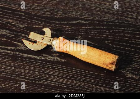 old dirty can opener on a wooden background Stock Photo