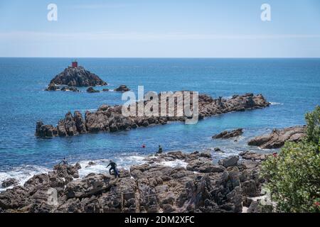 Tauranga New Zealand - December 2 2020; Divers on jagged rocky base to Mount Maunganui going into water in channel between base and rock island. Stock Photo