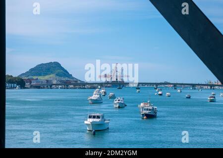 Landmark Mount Maunganui mit Hafen von Tauranga Containerkrane, Hafenbrücke und verankerte Boote von Eisenbahnbrücke eingerahmt von Stahlbrücke Struktur. Stockfoto