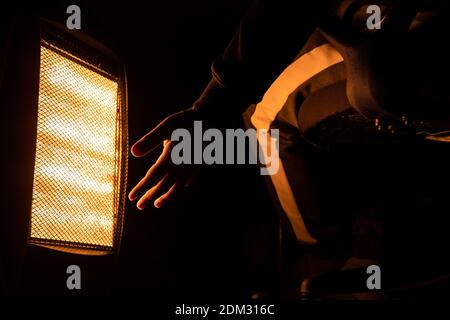 Nahaufnahme Hand eines Mannes mit Halogenheizung warm im Winter in schwarzem Hintergrund isoliert zu halten. Stockfoto