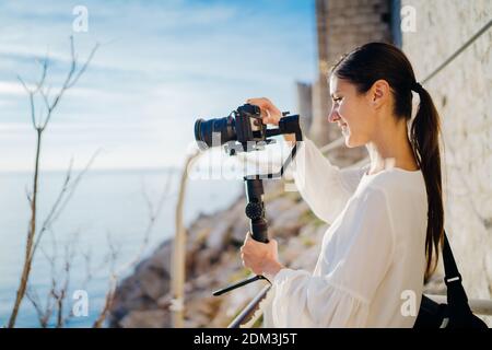 Lächelnd weibliche Reise Vlogger Video Creator Filmen mit einem spiegellosen Kamera auf einem Gimbal Stabilisator.Freelancer Frau Aufnahme eines niedrigen Budgets Film für ein Stockfoto