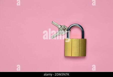 Goldenes geschlossenes Schloss mit Schlüsseln auf rosa Hintergrund. Speicherplatz kopieren. Draufsicht Stockfoto