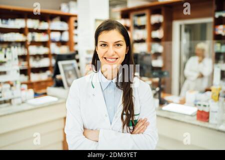 Smiling friendly pharmacist at the counter working in a pharmacy store. Pharmaceutical professional therapy recommendation. Giving advice about medica Stock Photo