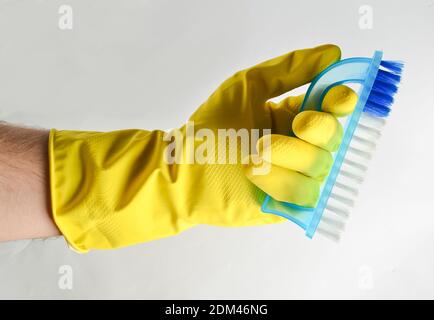 A man's hand in a yellow latex glove holds a plastic brush on a white background. Cleaning concept Stock Photo