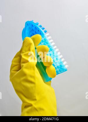 A man's hand in a yellow latex glove holds a plastic brush on a white background. Cleaning concept Stock Photo