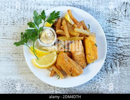 Knuspriger Fisch und Chips, serviert mit Mayonnaise und Zitrone auf einem Holztisch. Stockfoto