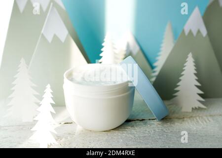 Kosmetische Creme auf blauem Hintergrund mit weihnachtsbäumen und Bergen. Winterpflege Stockfoto