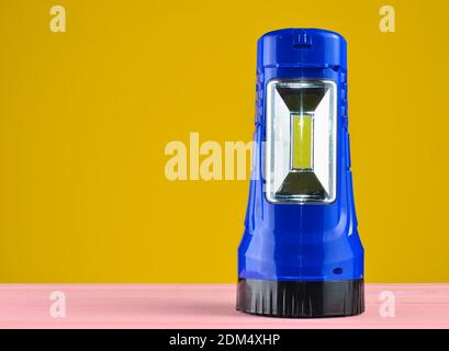 Blue flashlight projector lies on a desk isolated on a yellow wall Stock Photo