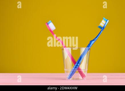 Two toothbrushes in a transparent plastic cup in the bathroom on a yellow background, copy space, minimalism Stockfoto