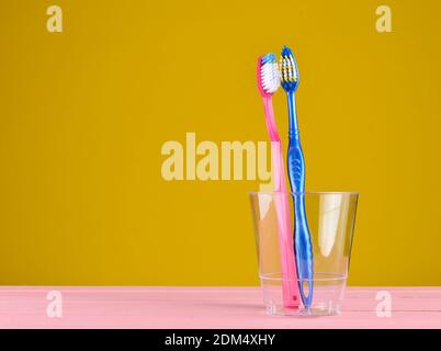 Two toothbrushes in a transparent plastic cup in the bathroom on a yellow background, copy space, minimalism Stockfoto