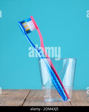 Zwei Zahnbürsten in einem transparenten Plastikbecher im Badezimmer auf blauem Hintergrund, Minimalismus Stockfoto