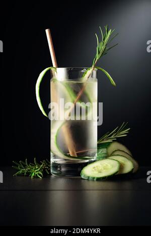 Kaltes Erfrischungsgetränk mit Eis, Gurke und Rosmarin. Das gefrorene Glas auf einem schwarzen Tisch. Stockfoto