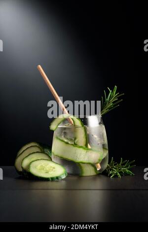 Kaltes Erfrischungsgetränk mit Eis, Gurke und Rosmarin. Das gefrorene Glas auf einem schwarzen Tisch. Stockfoto