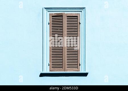 Graue Fensterläden am Fenster gegen eine blaue Wand. Altes Äußeres in italienischem oder griechischem Dorf mit geschlossenem Fenster. Stockfoto
