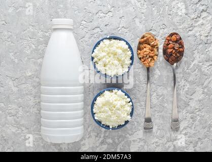 Gesunde, diätetische Lebensmittel. Frühstück am Morgen. Eine Flasche Joghurt, Schüsseln mit Hüttenkäse, Löffel mit Walnüssen und Rosinen auf einem grauen Betontisch. Oben Stockfoto