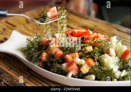 Person mit Gabel köstliche japanische Salat mit Trauben von Algen, Äpfel zu essen, und Tomaten. Stockfoto