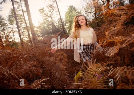 Eine junge, natürlich schöne Frau (20 Jahre) läuft durch die herbstlichen Farne, die sich an einem sonnigen Tag in einer Waldlandschaft mit einem Gefühl der Bewegung amüsieren. Stockfoto