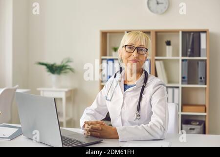 Portrait eines erfahrenen reiferen Arztes, der mit Laptop am Schreibtisch sitzt An ihrem Arbeitsplatz Stockfoto