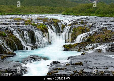 Eine Nahaufnahme des Bruarfoss Wasserfalls mit kaskadierenden blauen Wasser im Goldenen Kreis, Island. Pflanzen und Moos wachsen auf den Felsen rund um die Wasserfälle. Stockfoto