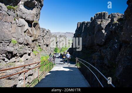 Besucher wandern entlang einer Promenade zwischen Haltepunkten in den Felsen, die durch die kontinentale Verschiebung, Thingvellir National Park erstellt wurden. Felsklippen säumen den Weg. Stockfoto