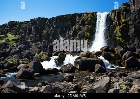 Oxararfoss, wie es Kaskaden über eine Basaltfelsenwand und große Felsbrocken an einem klaren sonnigen Tag im Thingvellir Nationalpark, Golden Circle, Island Stockfoto