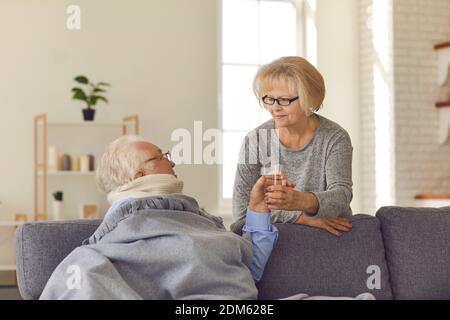 Fürsorgliche ältere Frau gibt einem Mann, der an Fieber und Halsschmerzen leidet, ein Glas Wasser. Stockfoto