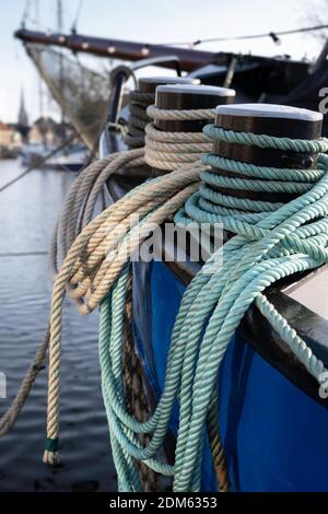 Dicke Schiffsseile um die Poller auf dem Bug eines Metallfrachters in Lemmer, Niederlande. Konzentrieren Sie sich auf die türkisfarbenen Seile. Enge Schärfentiefe Stockfoto
