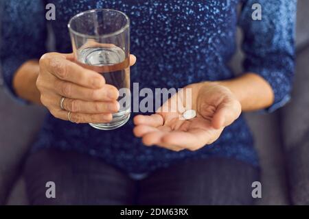 Nahaufnahme einer reifen Frau, die eine medizinische Pille mit einem Ein Glas Wasser, um ihre Schmerzen zu lindern Stockfoto