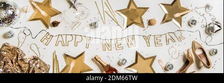 Flat-Lay von Happy New Year goldenen Schriftzug, Party Discoball, traditionelle goldene und silberne Glitzer Dekorationen, Schuhe, Kleid, Tasche und Champagner-Flasche auf weißem Hintergrund, Draufsicht. Layout für das neue Jahr Stockfoto