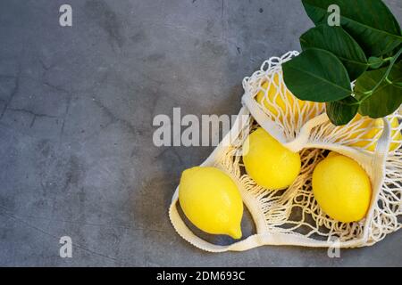 Reife frische Zitronen in weißer Saiten-Einkaufstasche auf grauem Hintergrund. Umweltfreundliches Essen, kein Plastik. Gesunde saubere Ernährung Konzepte. Stockfoto
