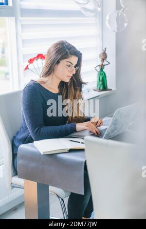 Eine junge hispanische Frau mit Brille, die am Computer arbeitet Im Büro Stockfoto