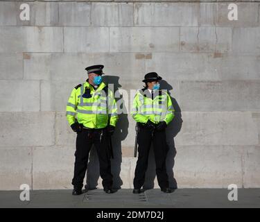 Trafalgar Square - London: Zwei Polizisten mit Gesichtsbezügen stehen vor der Wand der Nationalgalerie, während sich die Krise fortsetzt Stockfoto