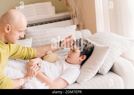 Ein fürsorglicher alleinerziehender Vater nimmt die Temperatur seines kranken Sohnes auf. Stockfoto