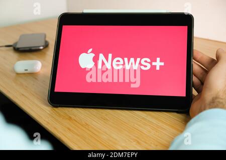 Apple News plus Logo auf dem Bildschirm des iPad Tablet Mit Smartphone iPhone Aufladen auf dem kabellosen Ladegerät und airpods im Gehäuse auf dem Hintergrund Stockfoto