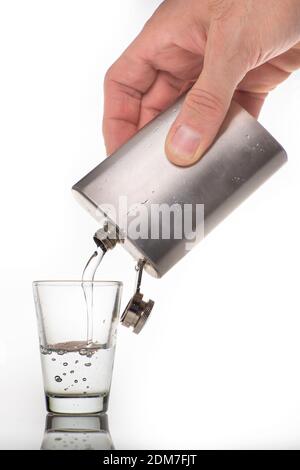 Gießen von hochprozentigem Alkohol in ein Glas-Shot-Glas. Metallflasche mit Alkohol und einem Glas Schnapsglas. Heller Hintergrund. Stockfoto