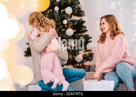 Glückliche Familie gibt ihrer Tochter Weihnachtsgeschenke. Das kleine Mädchen umarmt ihren Vater und freut sich über Geschenke Stockfoto