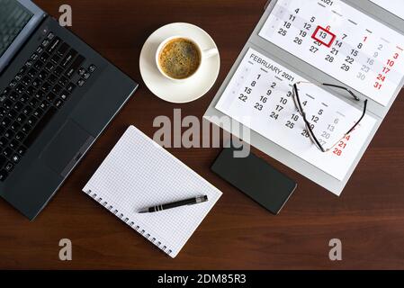 Draufsicht auf Büromaterial mit Laptop, Smartphone, Notizblock, Tasse Kaffee und Kalender Stockfoto