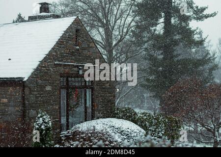 Ein Pflastersteinhaus mit einem Kranz in einem Fenster als nächstes Zu einer Suburban Straße während eines Schneesturms Stockfoto